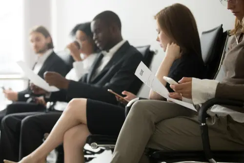 A group of business professionals sitting in a waiting area, each reviewing documents and using mobile devices.