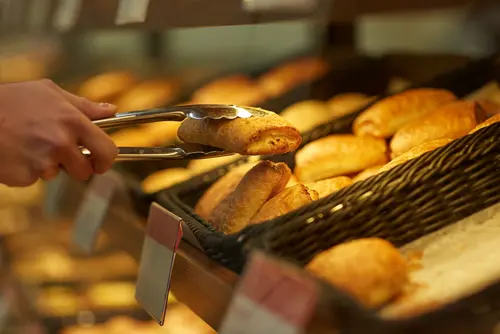 Freshly baked golden brown pastries displayed in a basket, with a hand picking one using tongs.